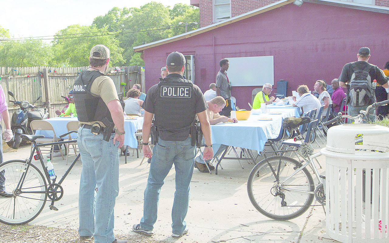 Law enforcement watches as homeless residents eat a meal prepared and served at Tampa Heights nonprofit the Well.