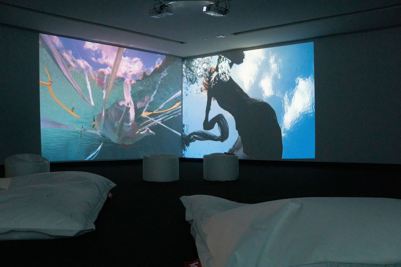 Chillax in a sea of dancing mermaids.
Head up to the second floor to see German-Brazilian artist Janaina Tschäpe’s “Blood, Sea,” which sounds far more foreboding than it is. The MFA nestled Tschäpe’s work in a dark room filled with floor pillows and bean bag chairs. Dancing mermaids, filmed at Weeki Wachee Springs, are projected onto the gallery walls, immersing the viewer in the underwater world of mermaids.