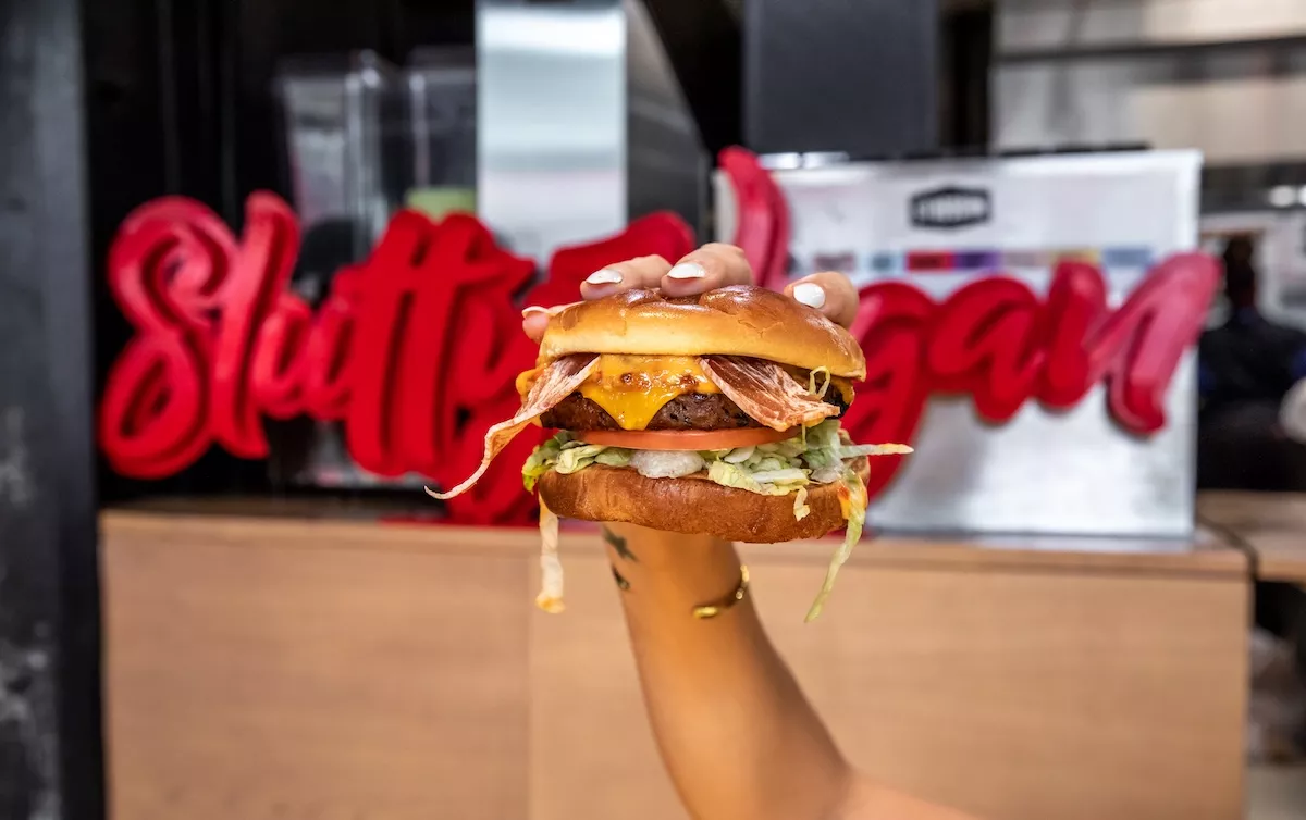 Slutty Vegan's 'One Night Stand' burger with a plant-based patty, Slutty Strips vegan bacon, vegan cheese, LTO, and Slut Sauce on a vegan Hawaiian bun.