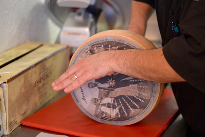 Bonano cuts into a wheel of grottino cheese in his Central Avenue deli. - Angelina Bruno