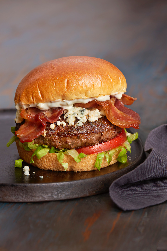 Burger 21's Black & Bleu piles on blue cheese sauce and crumbles, applewood-smoked bacon, Certified Angus beef, lettuce and tomato. - Burger 21