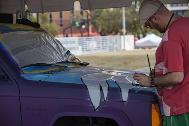 Derek Donnelley paints a Jeep for Carmada.  With Saturday's rains, Donnelley and partner Nate Baranowski had to make up for lost time, completing the art project on Sunday. - Kimberly DeFalco