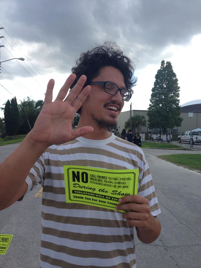 IN VIOLATION: Daniel Veintimilla poses for a cellphone pic holding one of the thousands of neon "No Cellphone" fliers papering the event. - NICOLE ABBETT