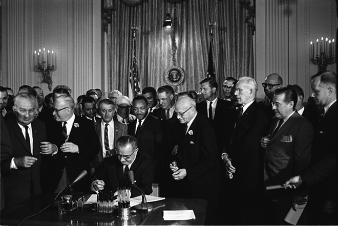 President Lyndon B. Johnson signs the Civil Rights Act of 1964. Martin Luther King, Jr.is among the many who are standing behind Johnson. - Wikimedia