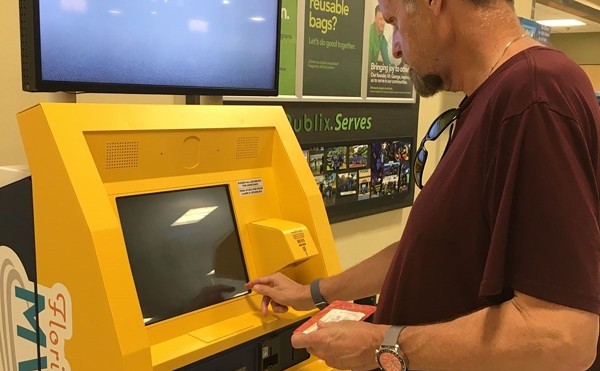 Person in maroon shirt operates yellow kiosk.