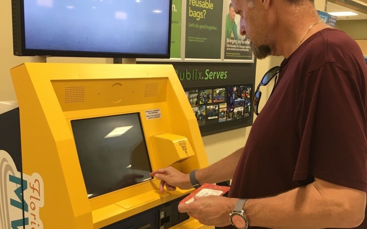 Person in maroon shirt operates yellow kiosk.